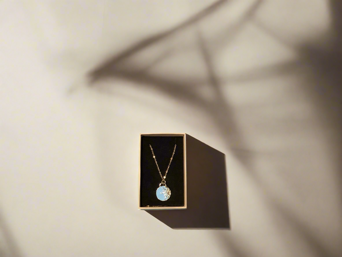 Necklace with enamel pale blue sun charm on a gold chain